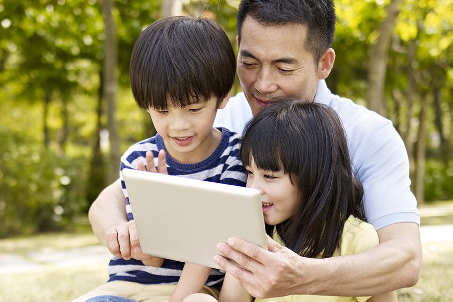 Client Center - Father and Two Children Using Their Tablet Outdoors in Front of Trees